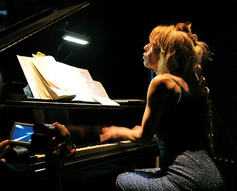 A female playing a grand piano under spotlight.